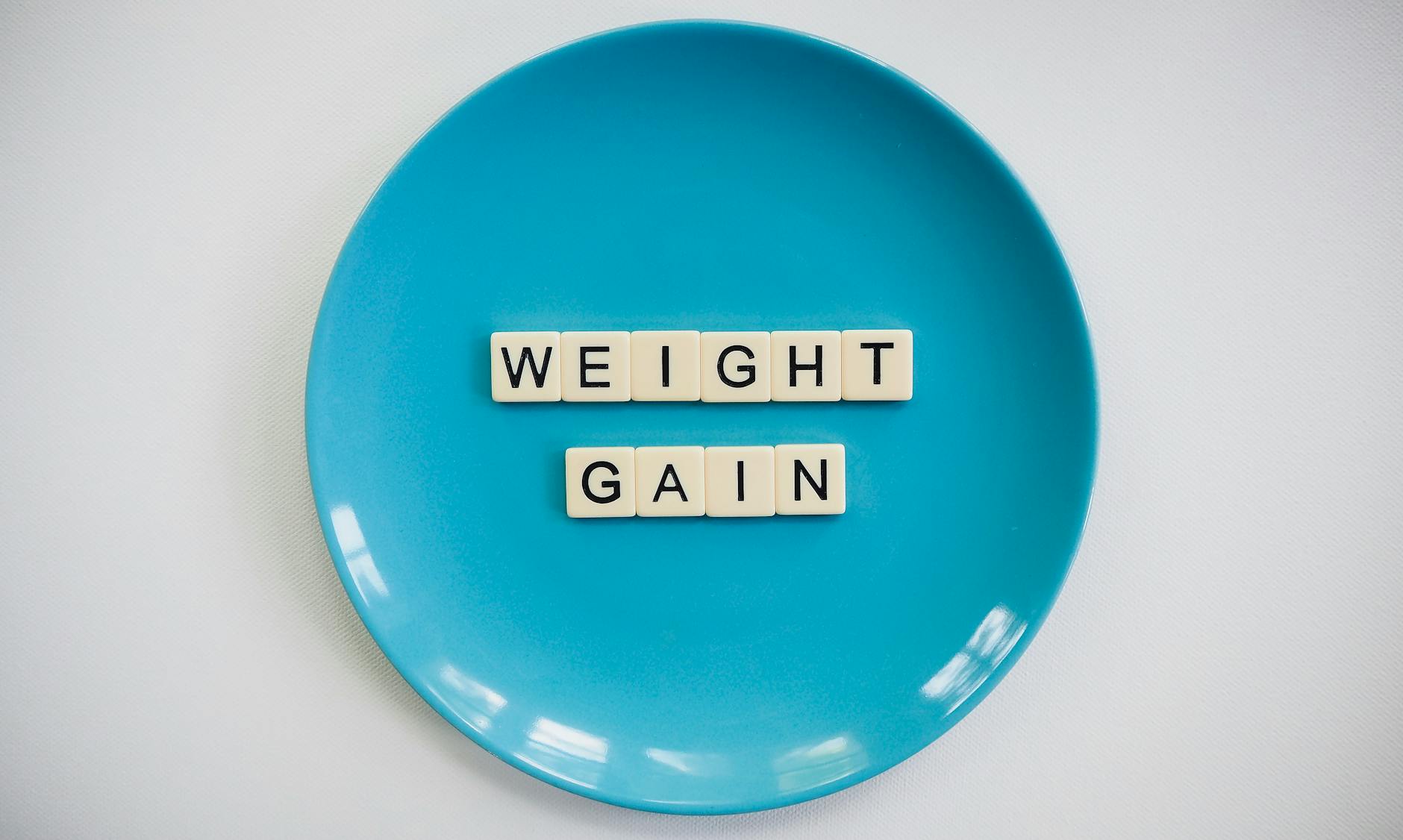 Płytki scrabble z napisem weight gain na niebieskim talerzu