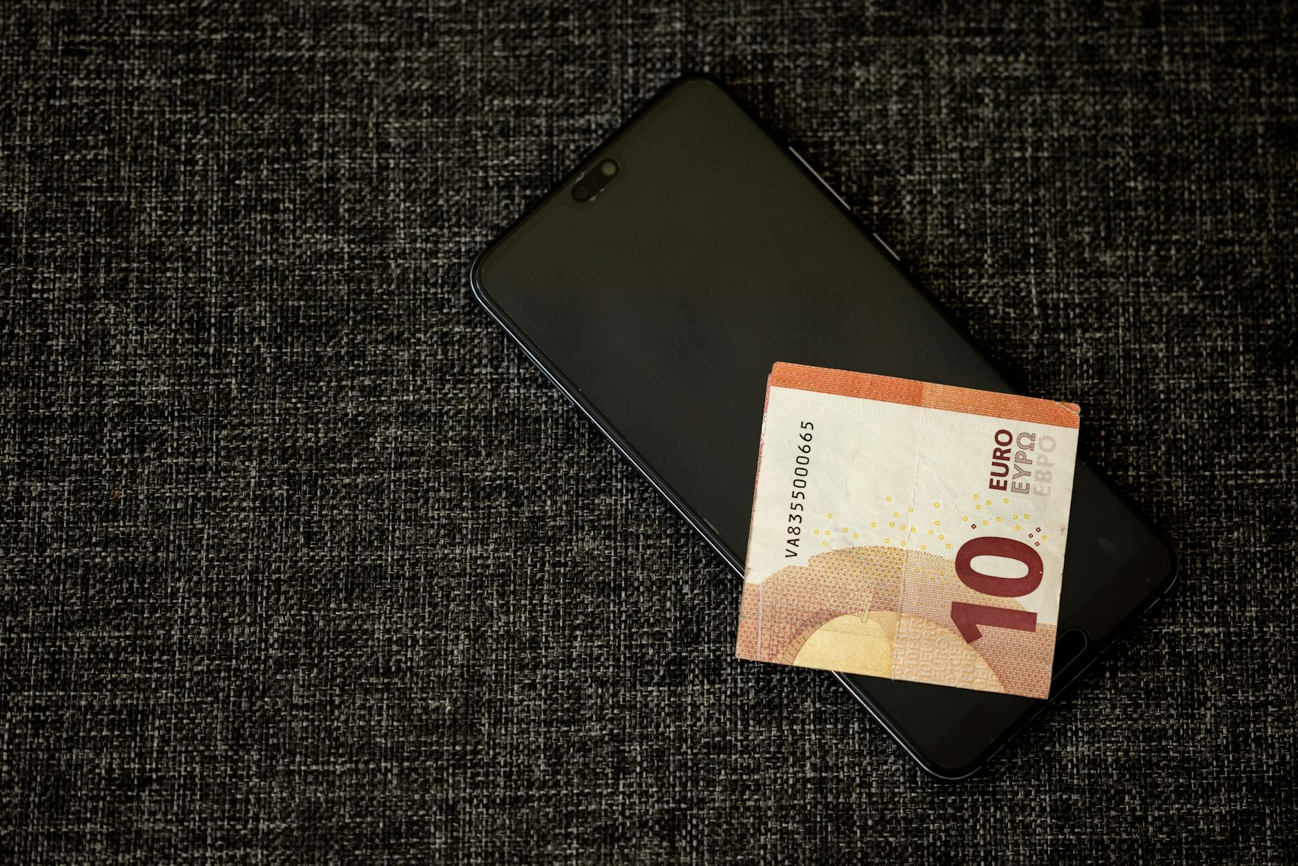 Banknot 10 euro leżący na smartfonie na ciemnym materiale