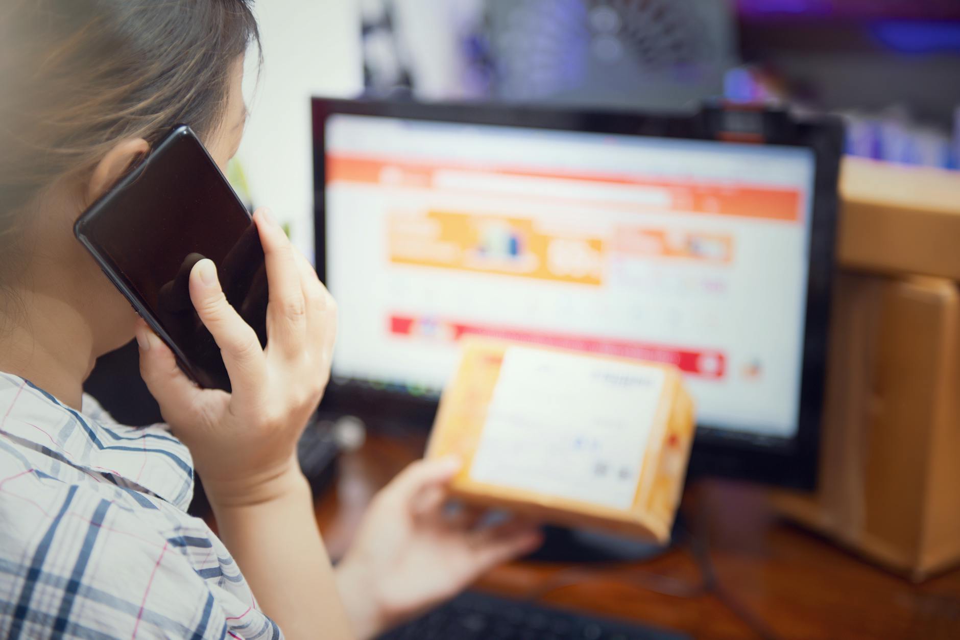 Kobieta w domu sprawdza paczkę z zamówieniem, trzymając telefon