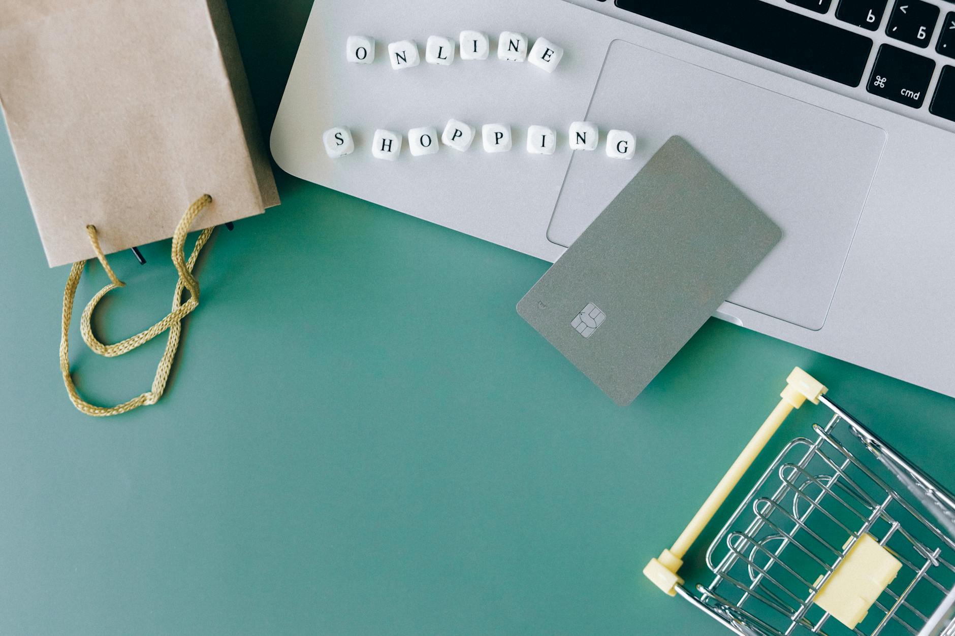 Laptop, karta płatnicza i miniwózek symbolizujące zakupy online