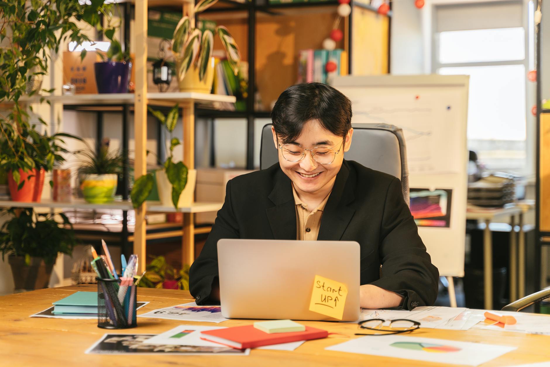 Specjalista w garniturze pracuje na laptopie przy biurku wśród roślin