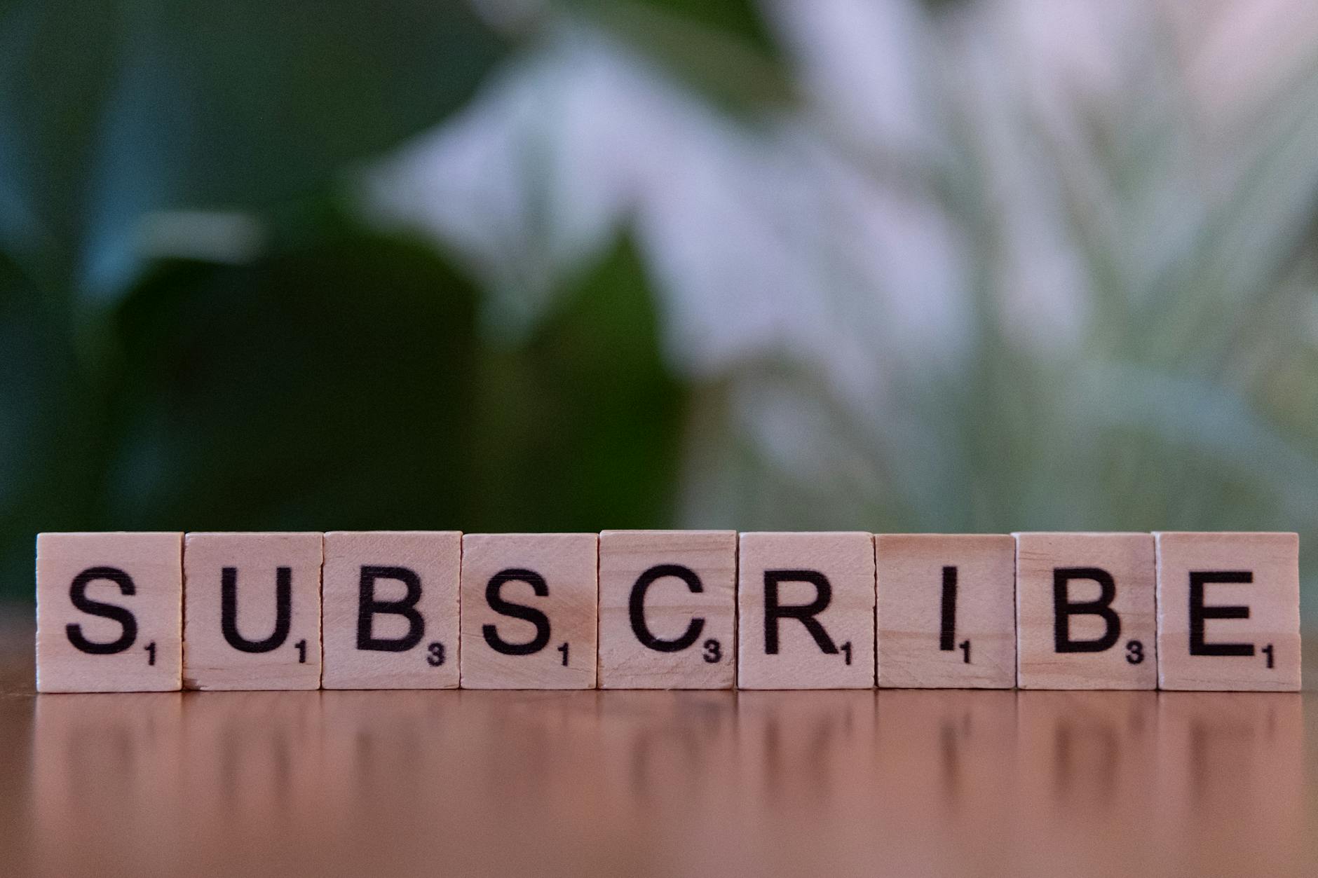Drewniane litery układające się w napis SUBSCRIBE na stole