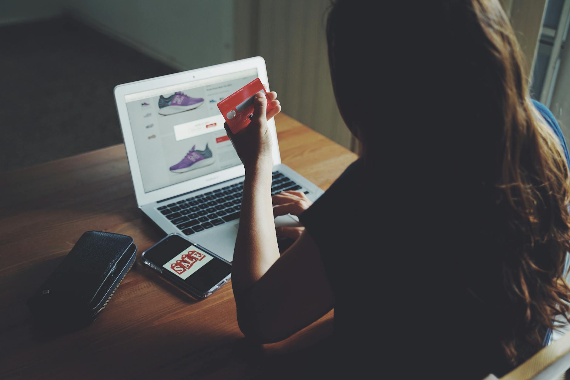 Kobieta płaci kartą za zakupy online na laptopie przy drewnianym stole