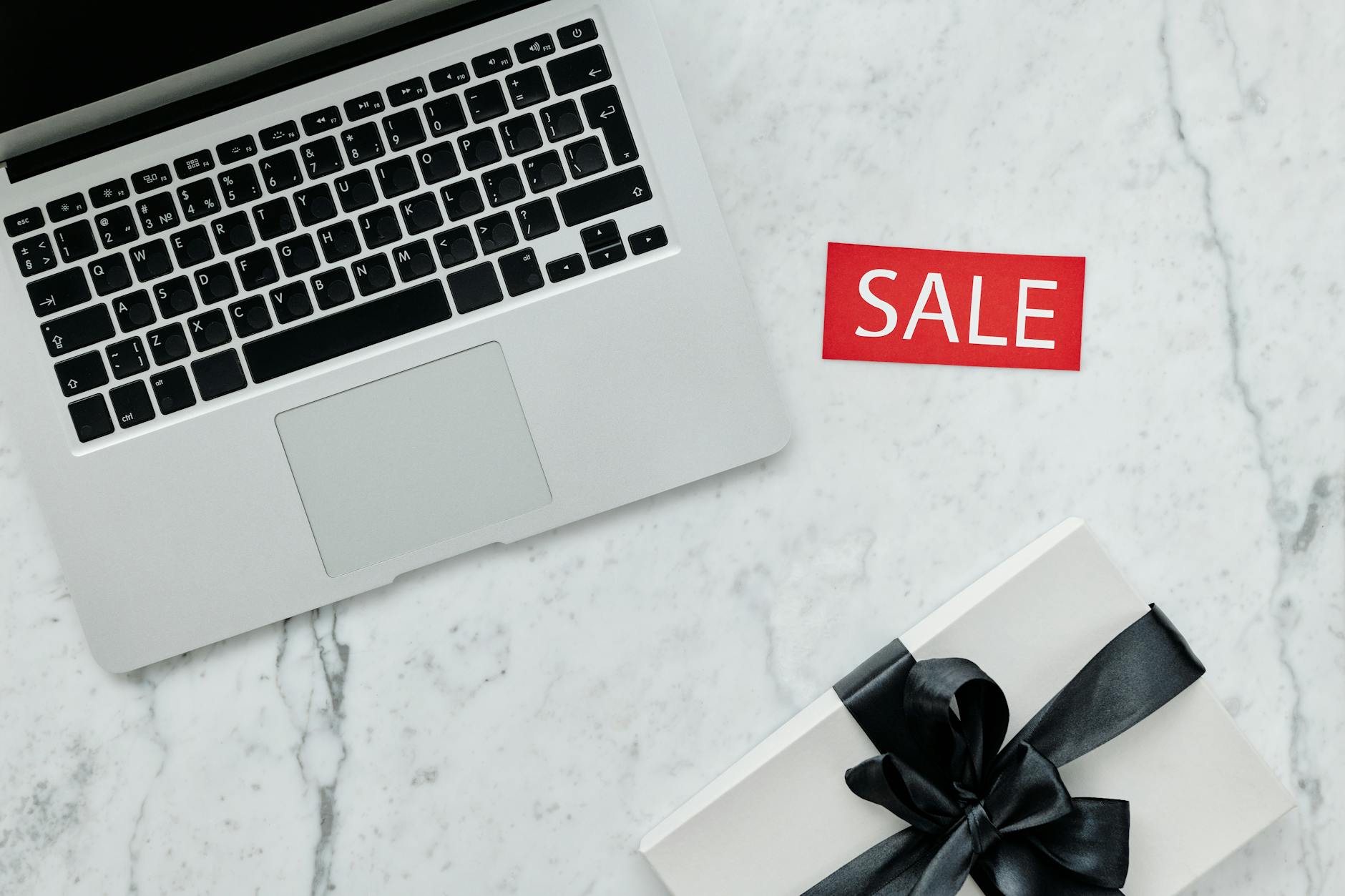 Laptop i zapakowany prezent z napisem sale na marmurowym blacie