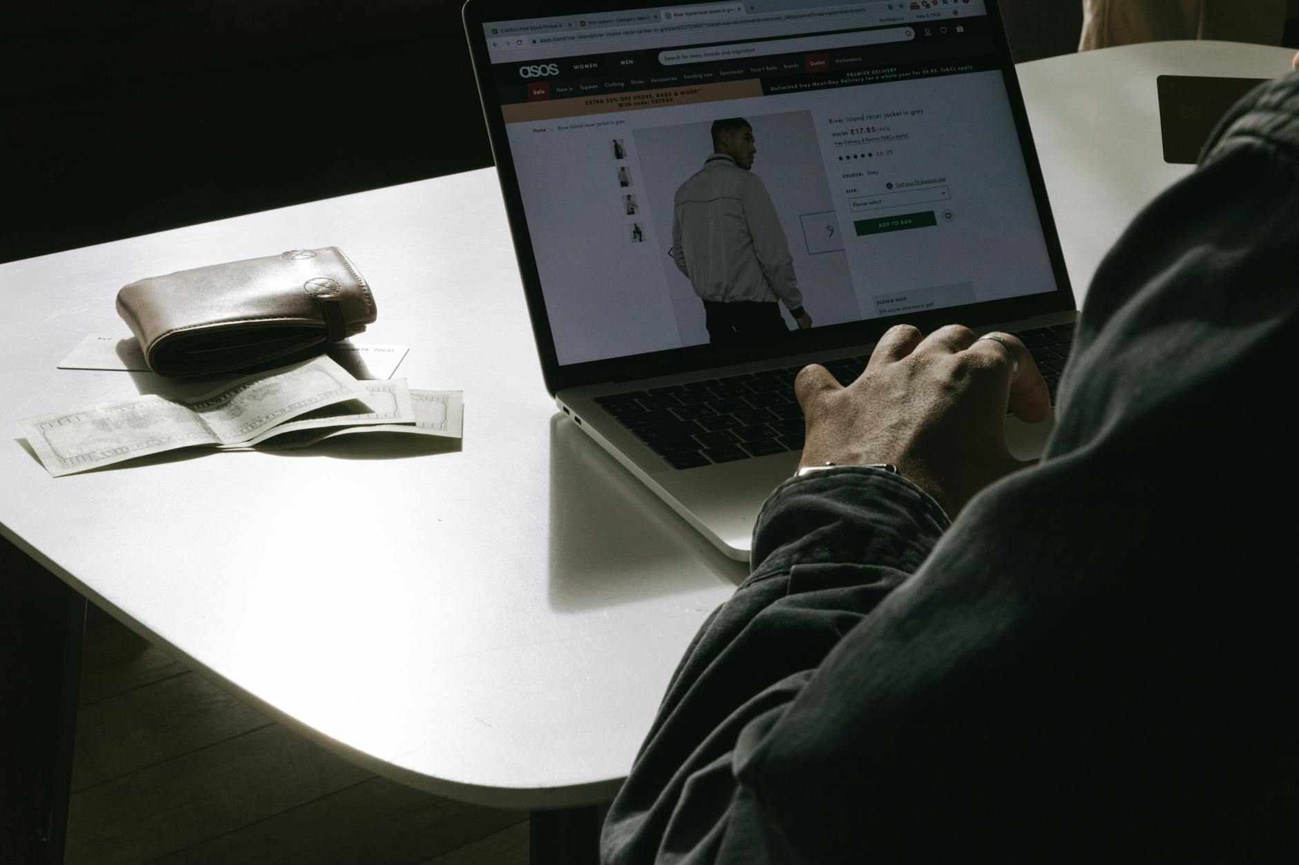 Mężczyzna robi zakupy online na laptopie, obok leży portfel