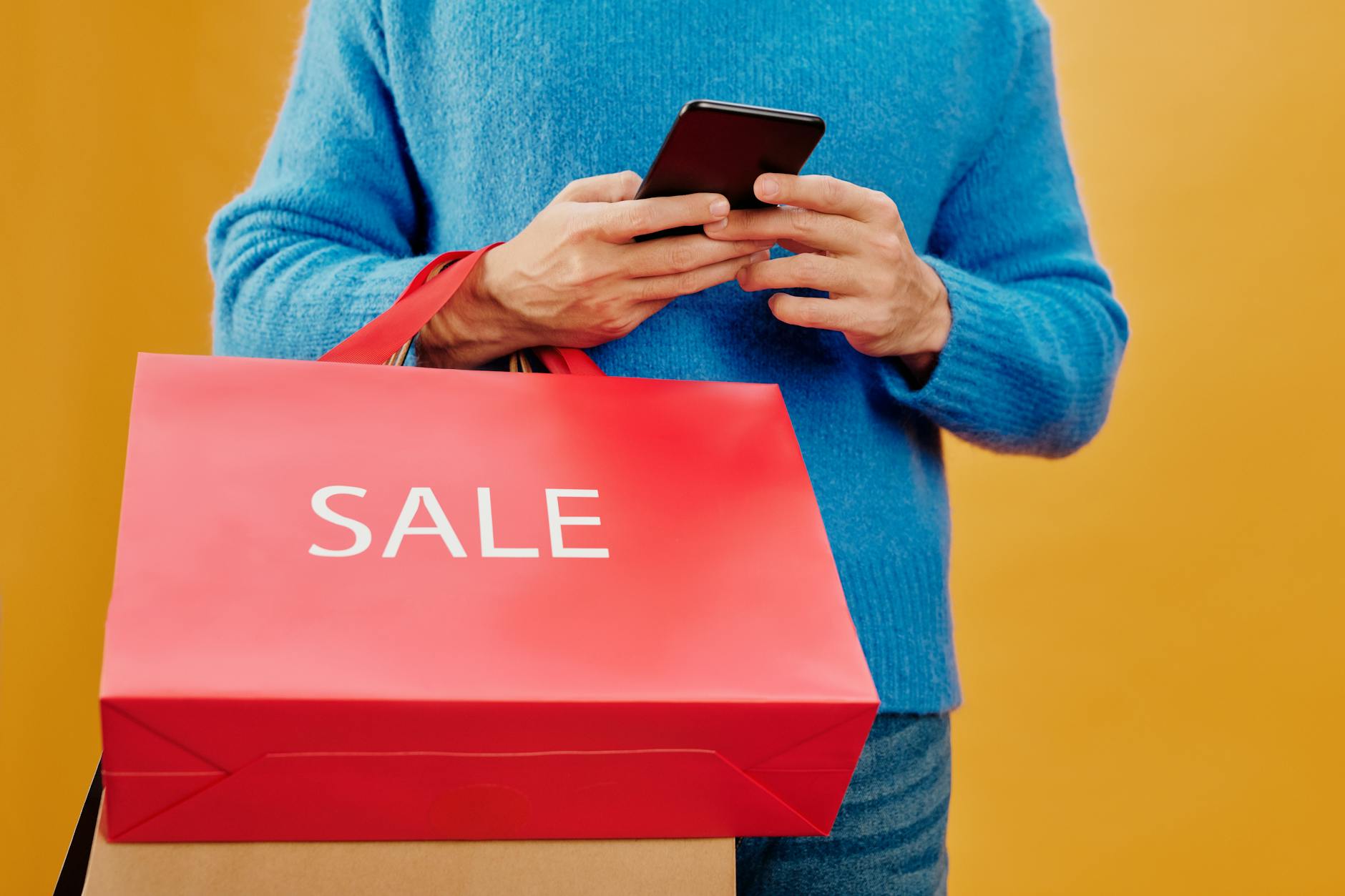 Mężczyzna z torbą z napisem sale i smartfonem, szukający okazji