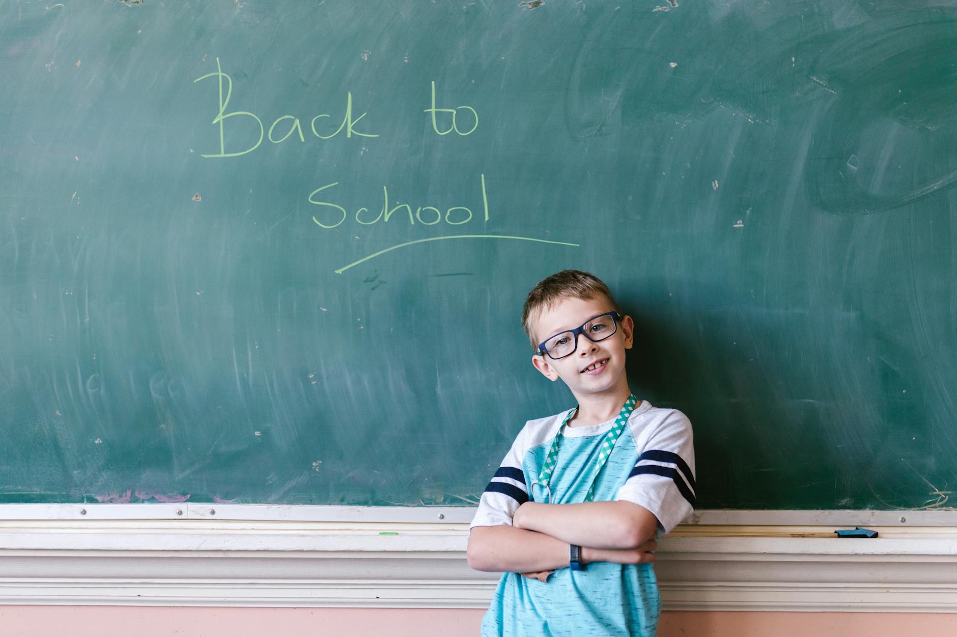 Chłopiec z założonymi rękami stoi przed tablicą z napisem Back to School