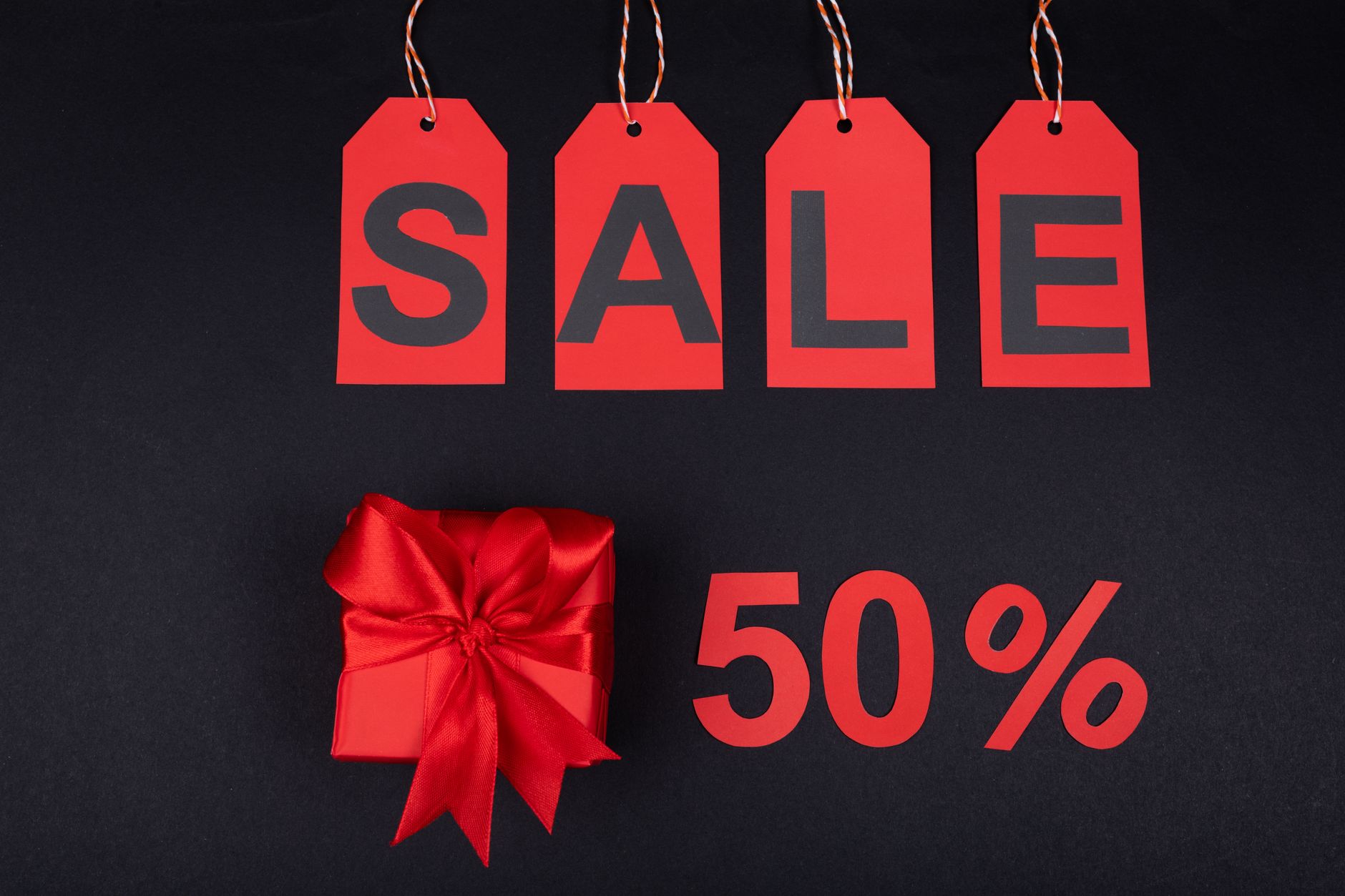 Czerwone pudełko prezentowe obok metek wyprzedaży i napisu -50%