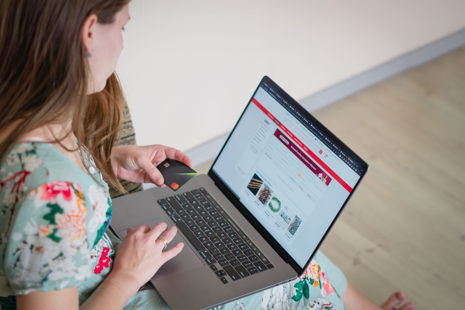 Kobieta w kwiecistej sukience robi zakupy online na laptopie z kartą