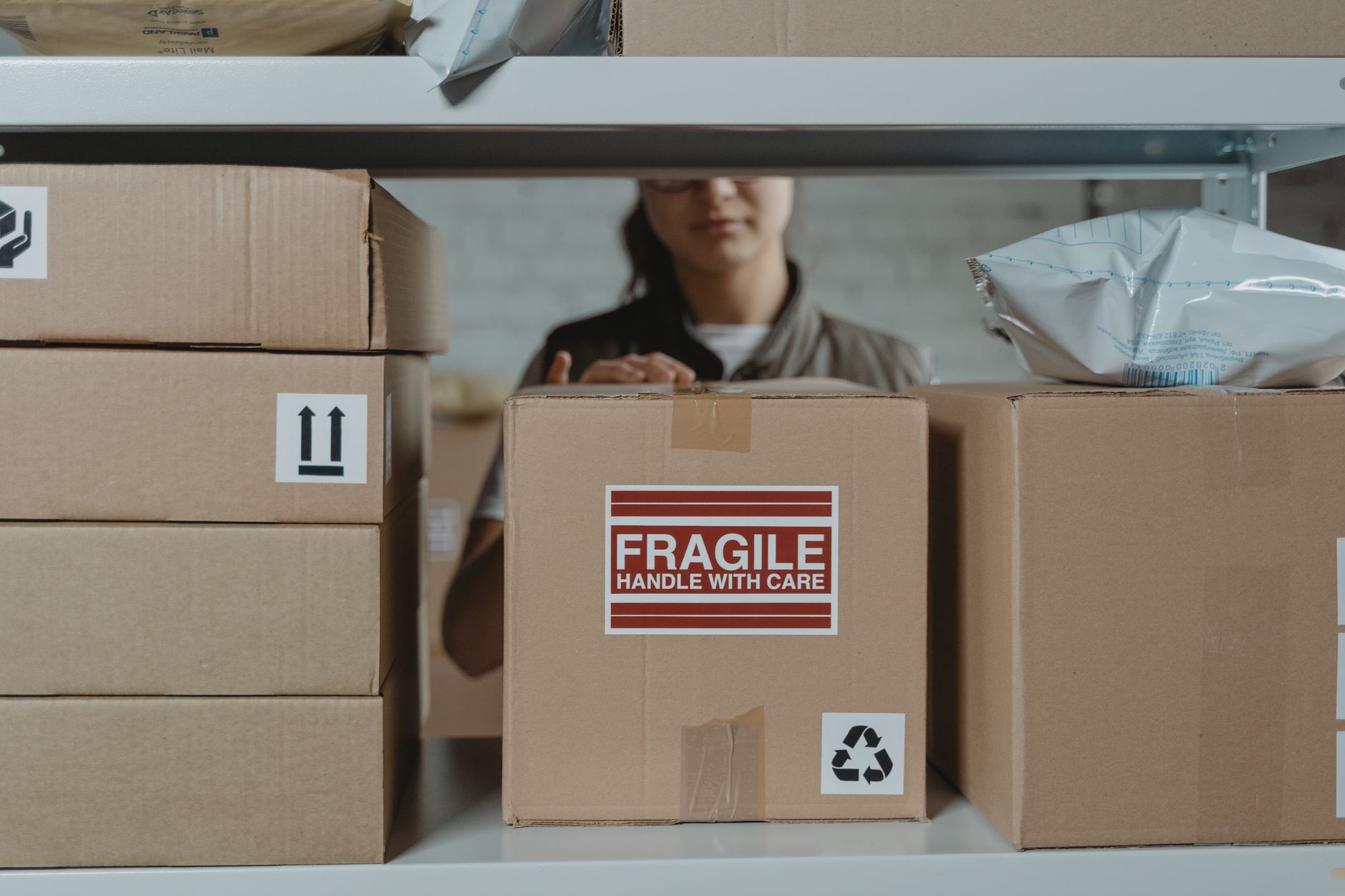 Pracownik w magazynie układa kartony z oznaczeniem ostrożnie Pracownik w magazynie układa kartony z oznaczeniem ostrożnie