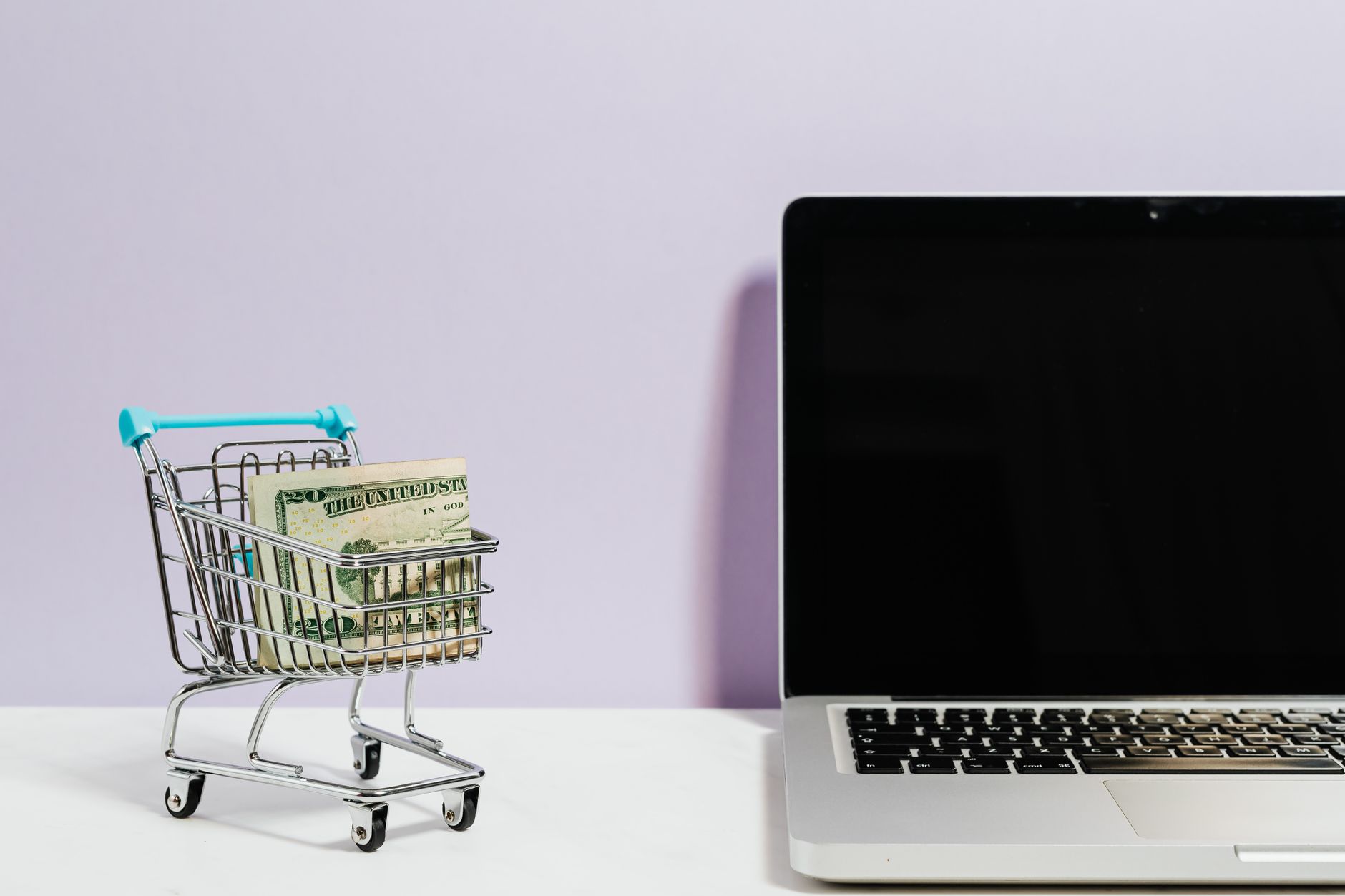 Wózek z plikami banknotów obok laptopa, zakupy online i oszczędzanie